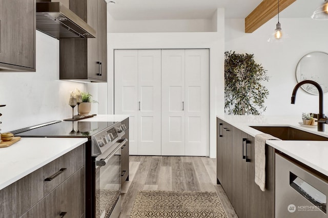 kitchen with stainless steel electric stove, sink, wall chimney range hood, pendant lighting, and light hardwood / wood-style flooring