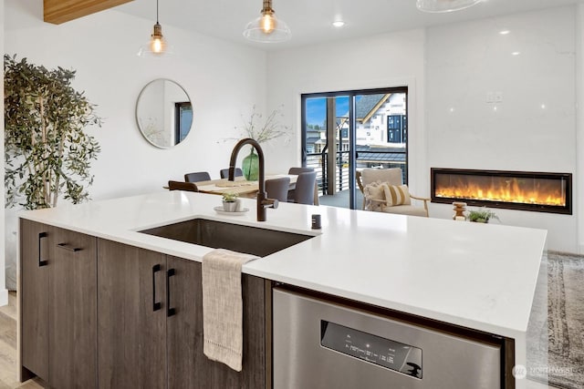 kitchen featuring a large fireplace, dark brown cabinetry, sink, pendant lighting, and light hardwood / wood-style flooring