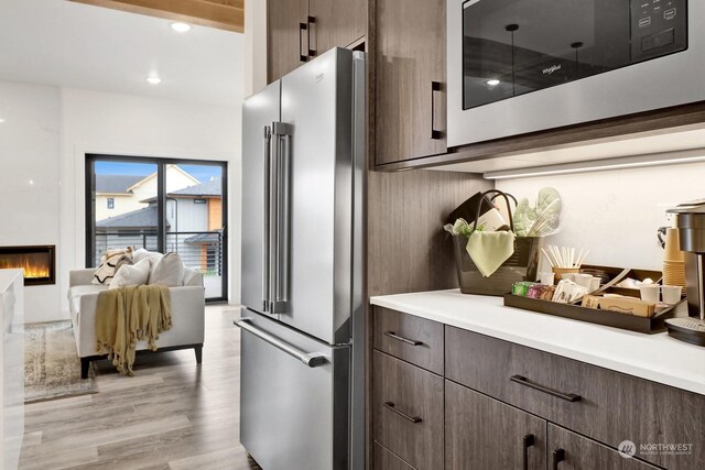205 Riverwalk Dr, Lynden, WA 98264 - kitchen featuring appliances with stainless steel finishes, light countertops, light wood-type flooring, a glass covered fireplace, and dark brown cabinets