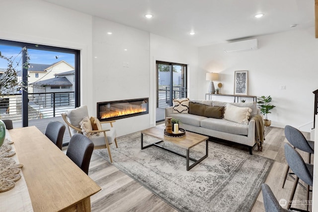 living room with an AC wall unit, a wealth of natural light, and light hardwood / wood-style flooring