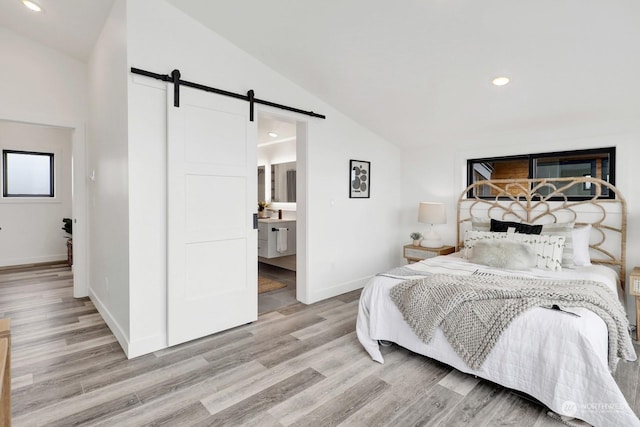 bedroom with light wood-type flooring, a barn door, lofted ceiling, and connected bathroom