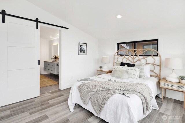 bedroom featuring a barn door, vaulted ceiling, and light hardwood / wood-style flooring