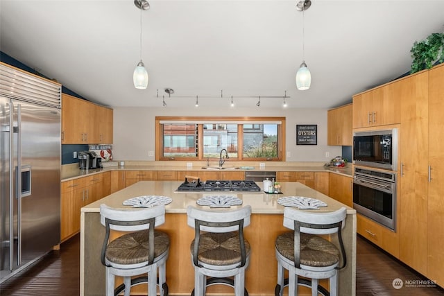 kitchen featuring sink, dark hardwood / wood-style flooring, built in appliances, pendant lighting, and a breakfast bar