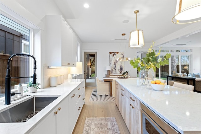 kitchen featuring built in microwave, sink, light hardwood / wood-style floors, decorative light fixtures, and white cabinets