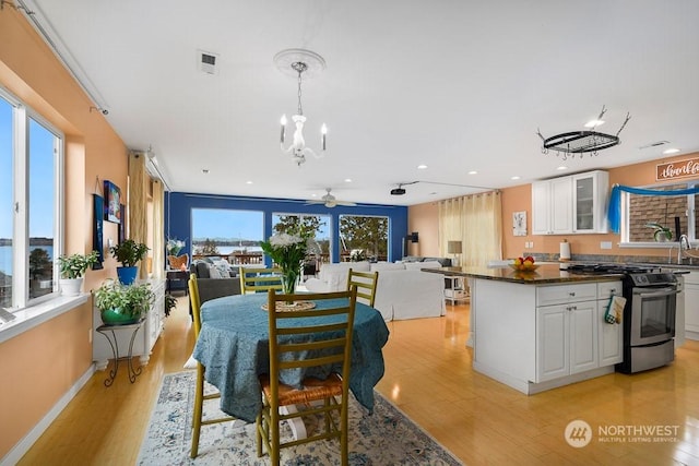 dining room with sink, a healthy amount of sunlight, ceiling fan with notable chandelier, and light hardwood / wood-style floors