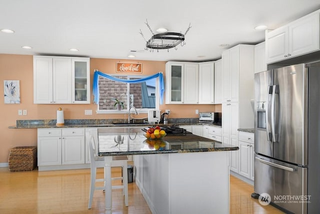 kitchen with a breakfast bar, dark stone counters, stainless steel fridge, light hardwood / wood-style floors, and white cabinetry