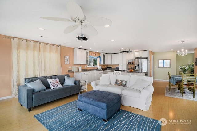 living room featuring ceiling fan with notable chandelier, light wood-type flooring, a wealth of natural light, and sink