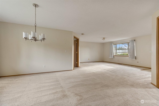 empty room with light colored carpet and an inviting chandelier