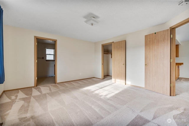 unfurnished bedroom with a textured ceiling, light carpet, connected bathroom, and a closet