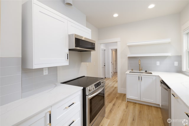 kitchen with light stone counters, stainless steel appliances, sink, white cabinets, and light hardwood / wood-style floors