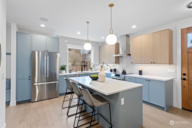 kitchen with stainless steel appliances, wall chimney range hood, pendant lighting, light hardwood / wood-style floors, and a kitchen island