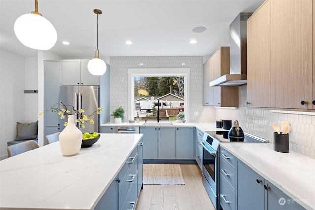 kitchen featuring pendant lighting, stainless steel appliances, light stone counters, and wall chimney exhaust hood