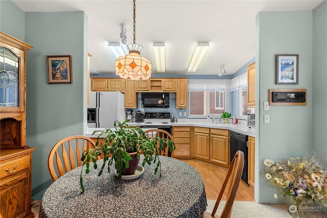 kitchen with light brown cabinetry, sink, decorative light fixtures, light hardwood / wood-style floors, and black appliances