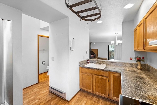 kitchen featuring light wood-type flooring, a baseboard heating unit, sink, an inviting chandelier, and hanging light fixtures