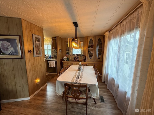 dining space with a textured ceiling, hardwood / wood-style flooring, an inviting chandelier, and wood walls