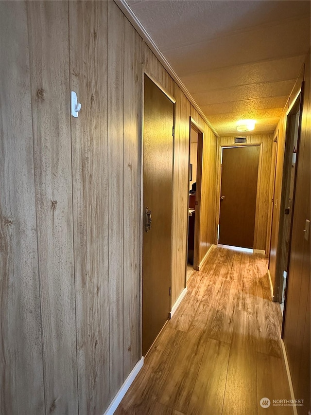 hallway featuring light wood-type flooring and wood walls