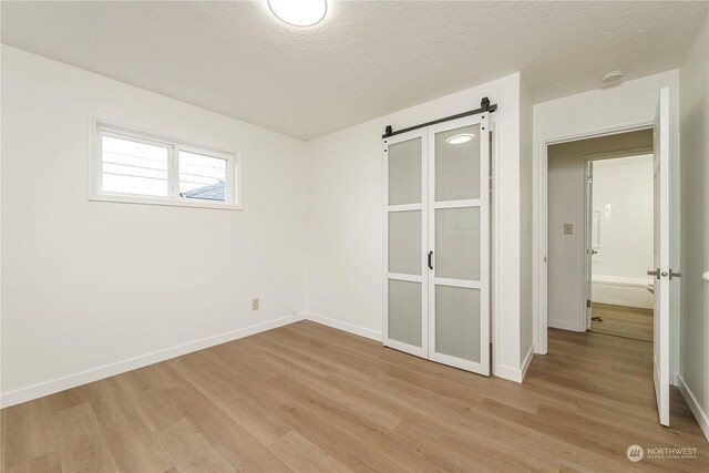 spare room with a barn door, a textured ceiling, and light hardwood / wood-style flooring