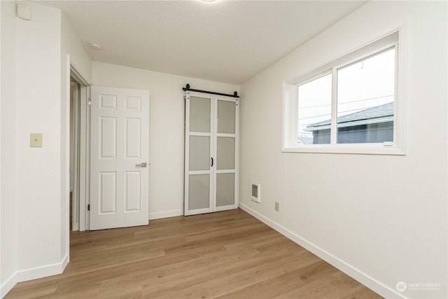 unfurnished bedroom with a barn door and light hardwood / wood-style floors