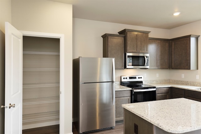 kitchen featuring light stone countertops, wood-type flooring, stainless steel appliances, and dark brown cabinets