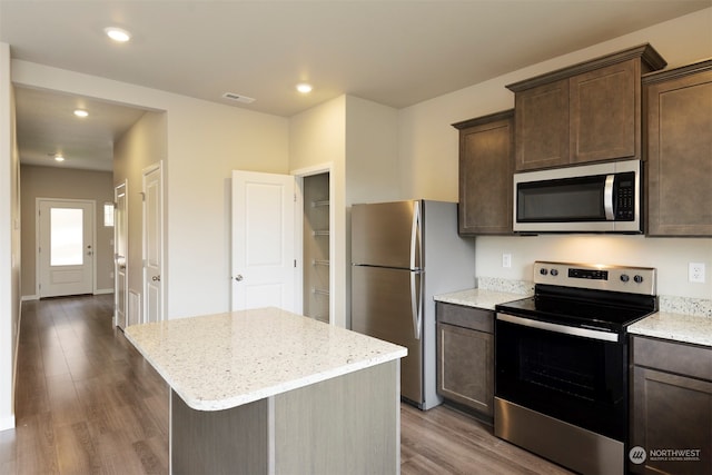 kitchen with appliances with stainless steel finishes, a center island, light stone counters, and dark wood-type flooring