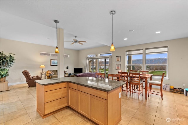 kitchen with light brown cabinets, dark stone counters, hanging light fixtures, ceiling fan, and light tile patterned floors