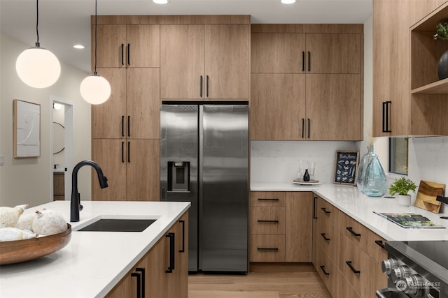 kitchen featuring light wood-type flooring, stainless steel fridge with ice dispenser, sink, and hanging light fixtures