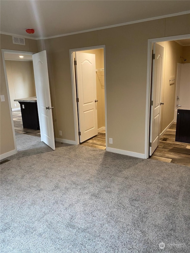 unfurnished bedroom with ornamental molding, a spacious closet, a closet, and dark wood-type flooring