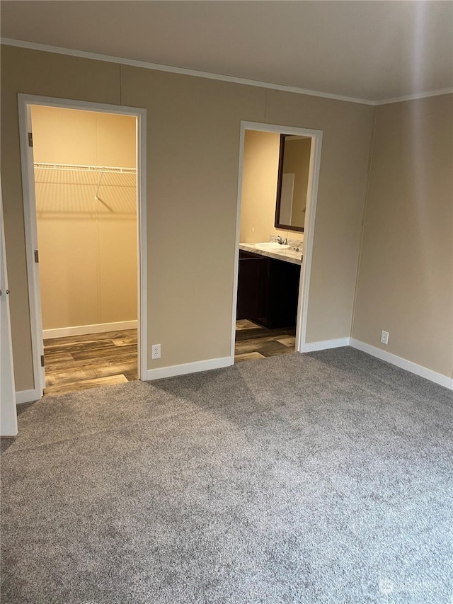 unfurnished bedroom with carpet flooring, a spacious closet, crown molding, and a closet