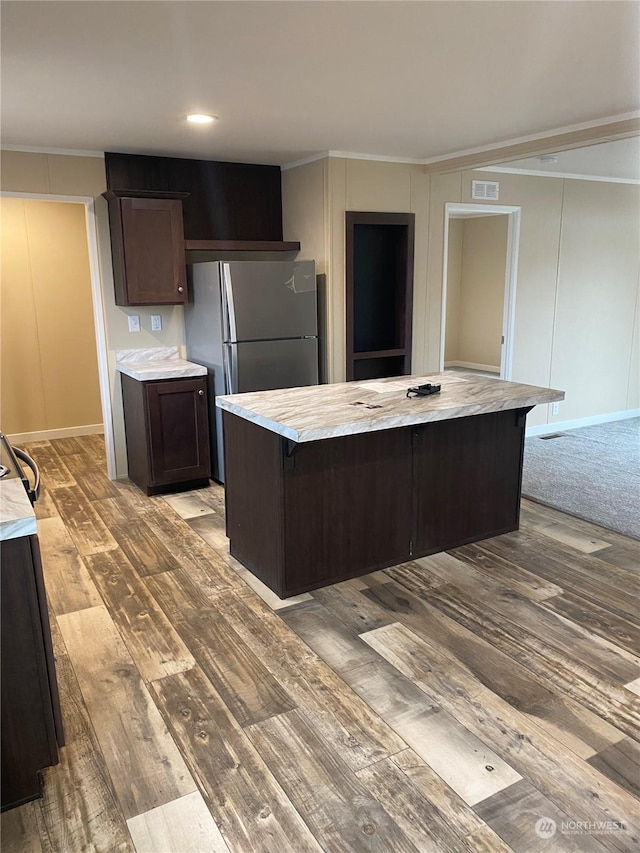 kitchen with stainless steel fridge, light wood-type flooring, dark brown cabinetry, a kitchen island, and a breakfast bar area