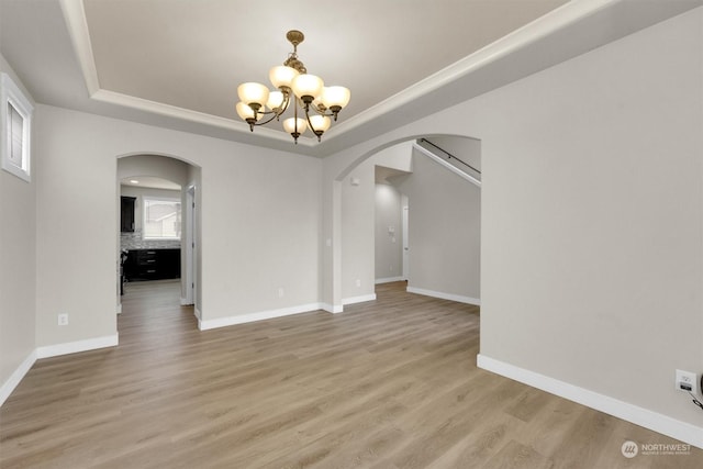 unfurnished room with wood-type flooring, a tray ceiling, and an inviting chandelier