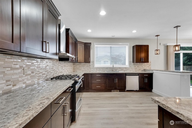 kitchen with sink, hanging light fixtures, stainless steel appliances, light stone counters, and light hardwood / wood-style flooring