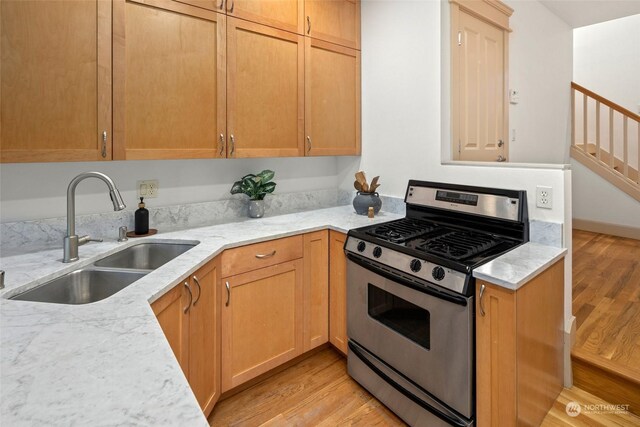 kitchen with light stone countertops, sink, light wood-type flooring, and stainless steel range with gas stovetop