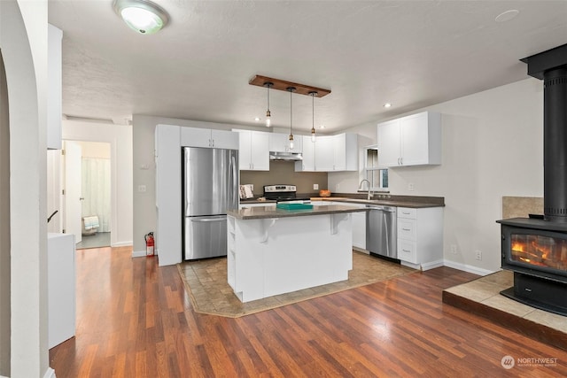 kitchen featuring stainless steel appliances, white cabinetry, a center island, dark hardwood / wood-style floors, and a wood stove