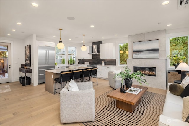 living room featuring a tile fireplace, light hardwood / wood-style floors, a wealth of natural light, and sink