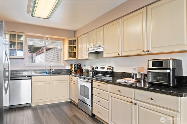 kitchen with stainless steel appliances, dark wood-style floors, a sink, glass insert cabinets, and under cabinet range hood