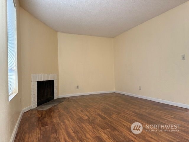 unfurnished living room with a textured ceiling, a fireplace, and dark wood-type flooring