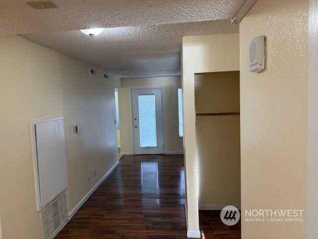 hall with a textured ceiling and dark hardwood / wood-style floors