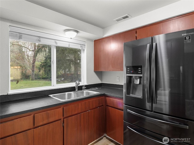 kitchen with stainless steel fridge, visible vents, dark countertops, brown cabinets, and a sink