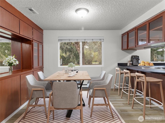 dining room featuring light wood finished floors, a baseboard radiator, visible vents, and a healthy amount of sunlight