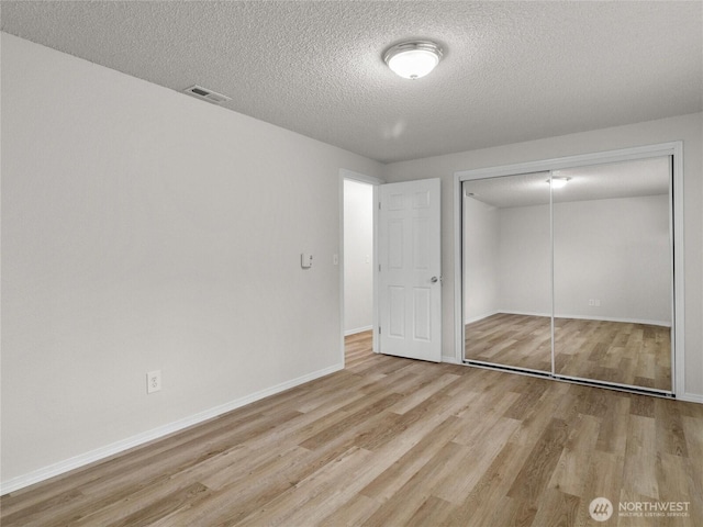 unfurnished bedroom with a textured ceiling, visible vents, baseboards, a closet, and light wood-type flooring