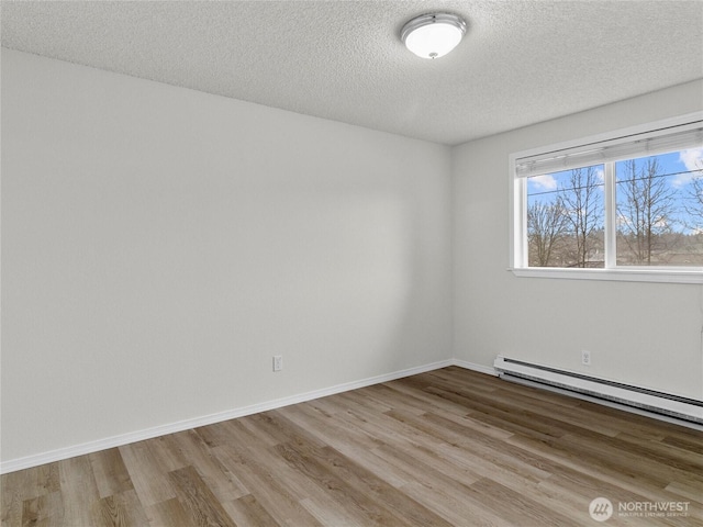 spare room featuring a baseboard heating unit, light wood-type flooring, a textured ceiling, and baseboards