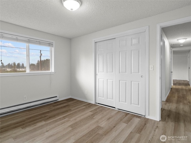 unfurnished bedroom with a textured ceiling, a baseboard heating unit, baseboards, light wood-style floors, and a closet