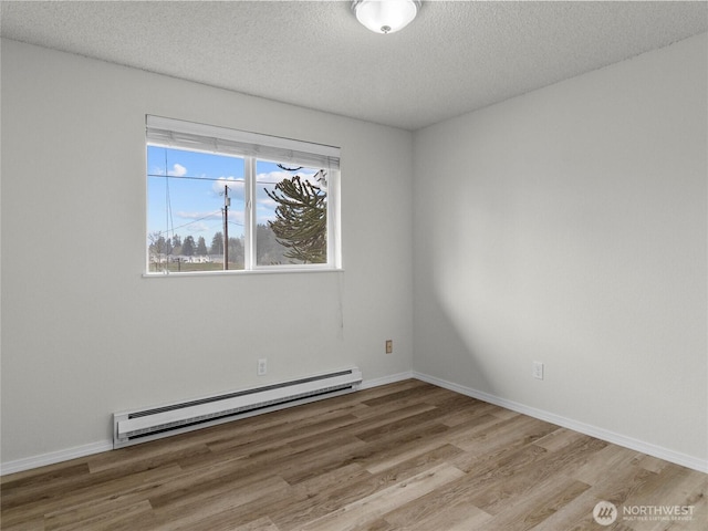 spare room with a baseboard heating unit, a textured ceiling, wood finished floors, and baseboards