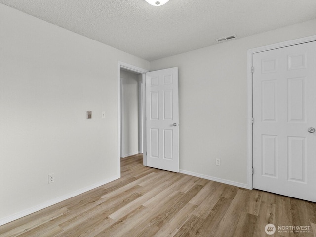 unfurnished bedroom featuring light wood-type flooring, visible vents, a textured ceiling, and baseboards