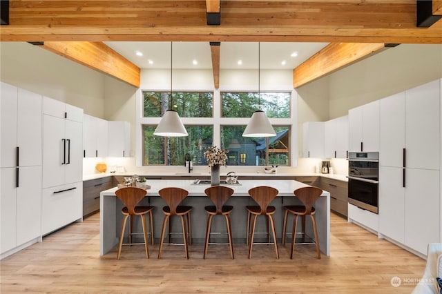 kitchen featuring beam ceiling, white cabinetry, an island with sink, and pendant lighting