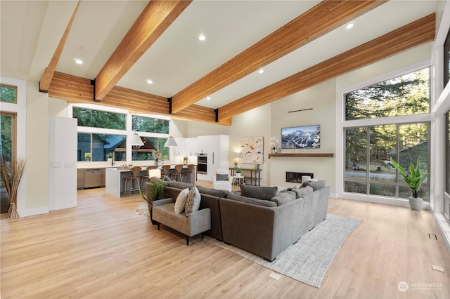 living room with beamed ceiling, a high ceiling, and light wood-type flooring