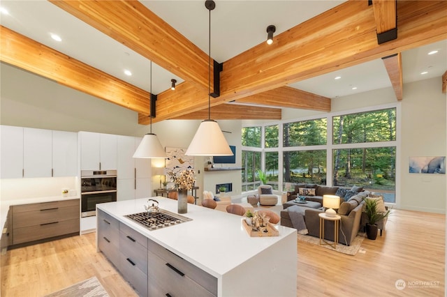 kitchen featuring a center island, hanging light fixtures, white cabinetry, beam ceiling, and stainless steel double oven