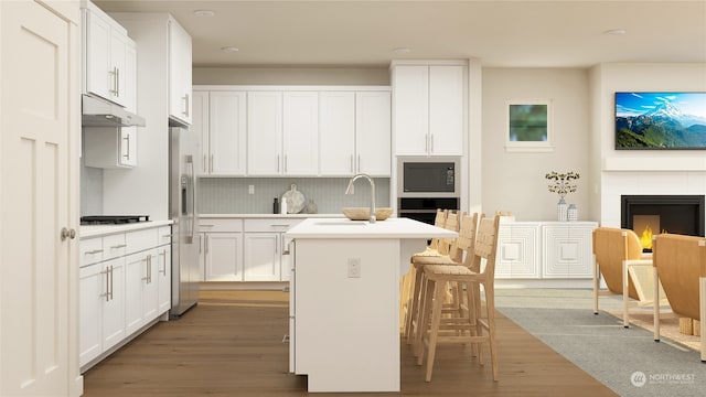 kitchen with a center island with sink, white cabinets, sink, wood-type flooring, and a tiled fireplace