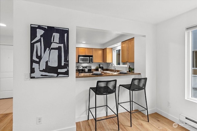 kitchen with sink, stainless steel appliances, baseboard heating, a breakfast bar area, and light wood-type flooring