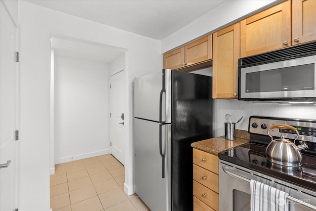 kitchen featuring light tile patterned floors, dark stone counters, and appliances with stainless steel finishes